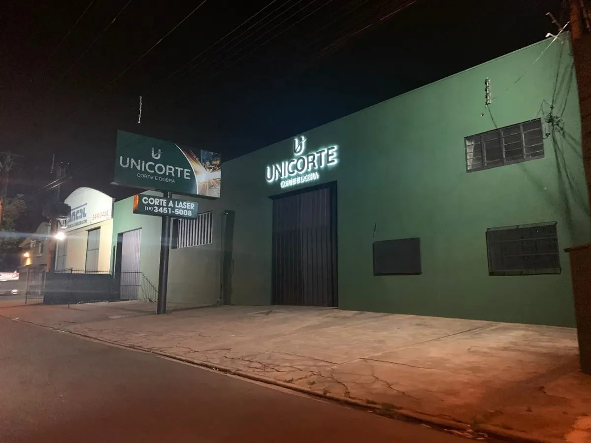 Fachada do galpão Unicorte à noite com letreiro Corte e Dobra iluminado